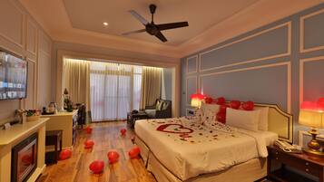 A hotel room with a large bed, a ceiling fan, a TV, a desk, and a fireplace.