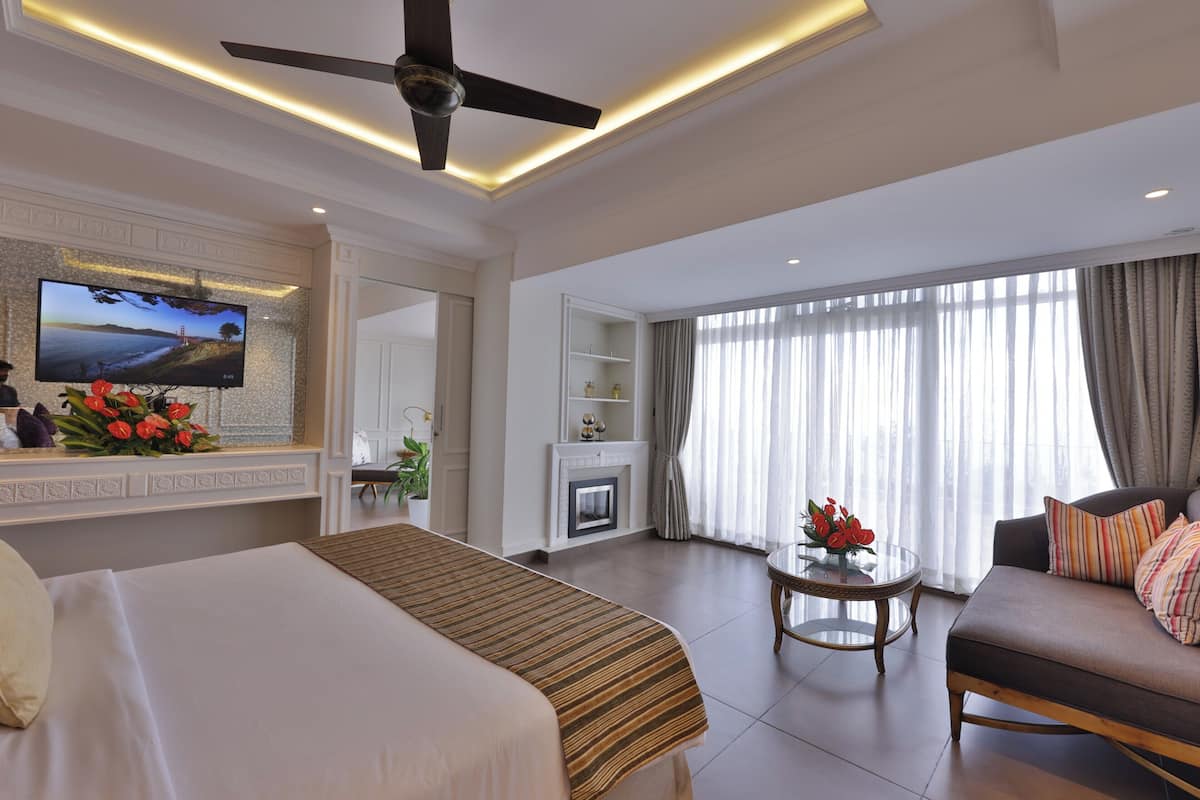 A hotel room with a bed, a sofa, a television, a fireplace, and a ceiling fan.