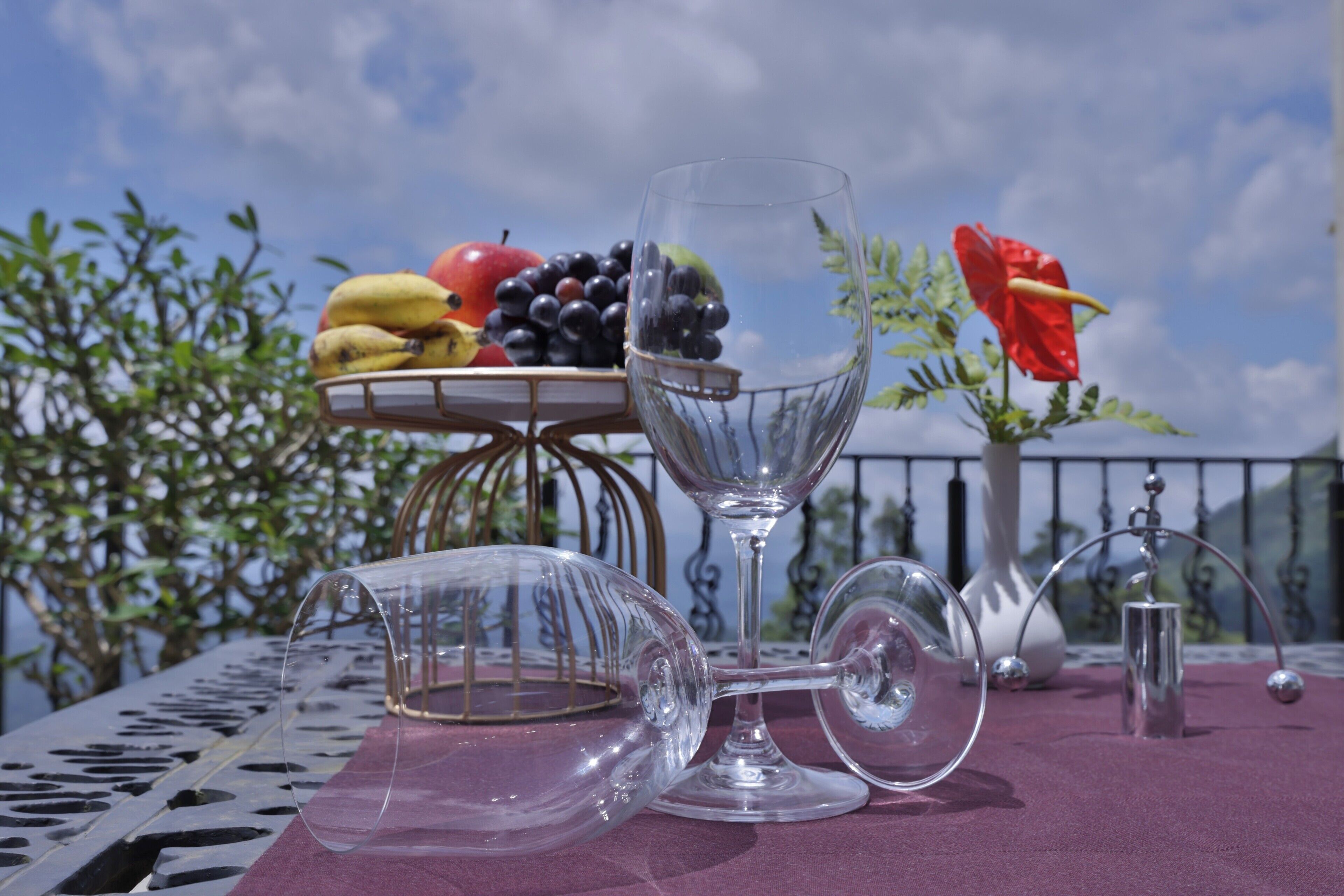 A table with a glass pitcher, a wine glass, and a fruit basket containing bananas, grapes, and an apple.