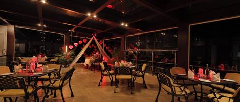 Un restaurante con mesas y sillas de madera, una estructura decorativa central y ventanas amplias.