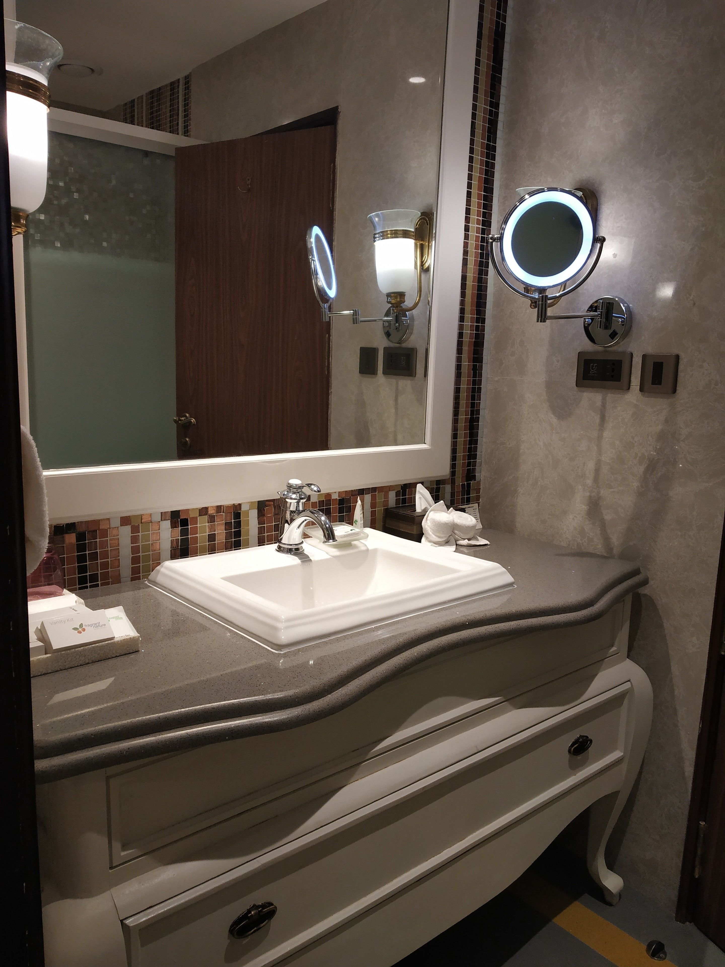 A bathroom with a large mirror, a white sink, and a vanity with drawers.