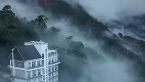 Un edificio de varios pisos con un diseño arquitectónico moderno, rodeado de montañas cubiertas de niebla.