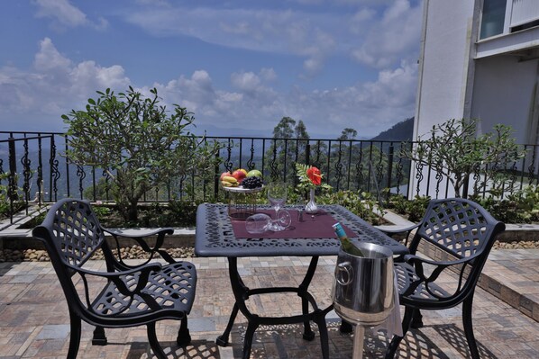An outdoor patio with a table set for two, a bottle of champagne, and a fruit bowl.