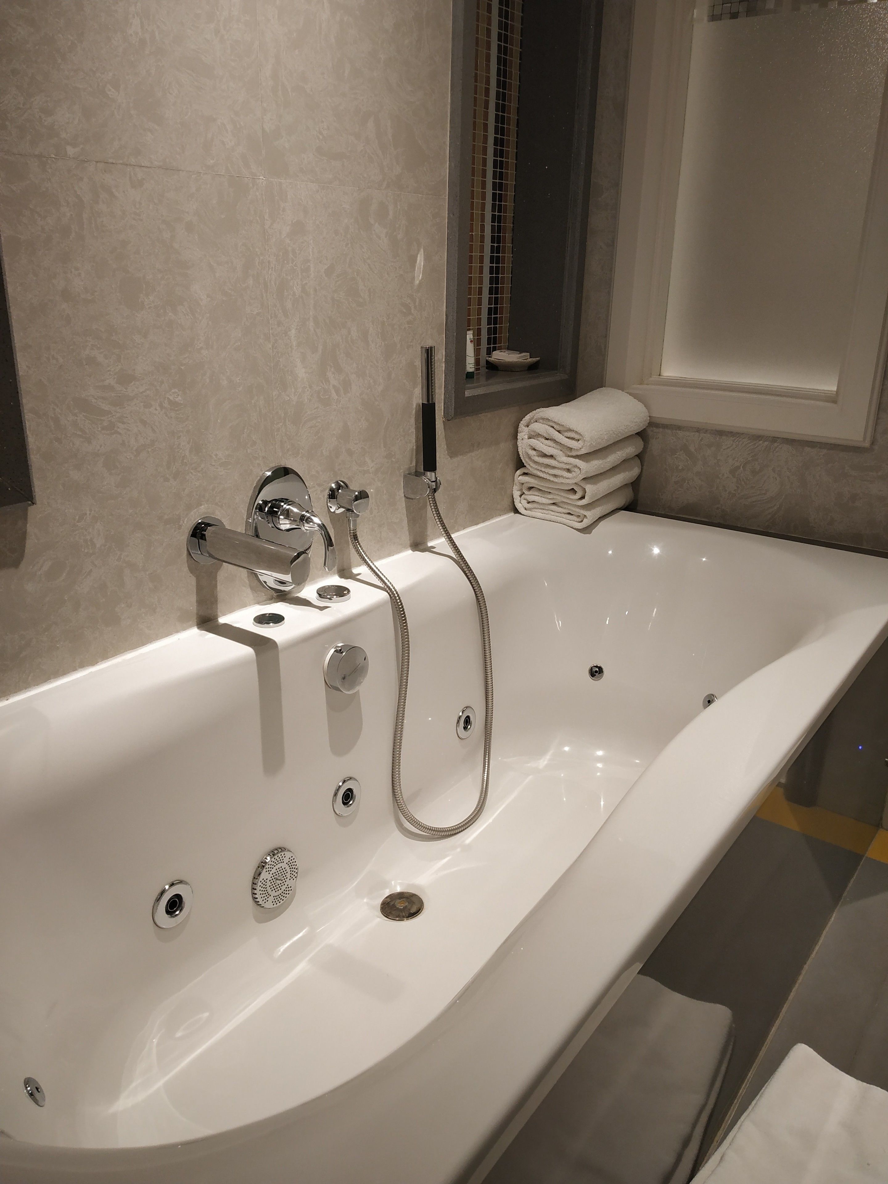A modern bathroom with a large bathtub, a handheld showerhead, and a stack of neatly folded towels.