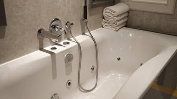 A modern bathroom with a large bathtub, a handheld showerhead, and a stack of neatly folded towels.