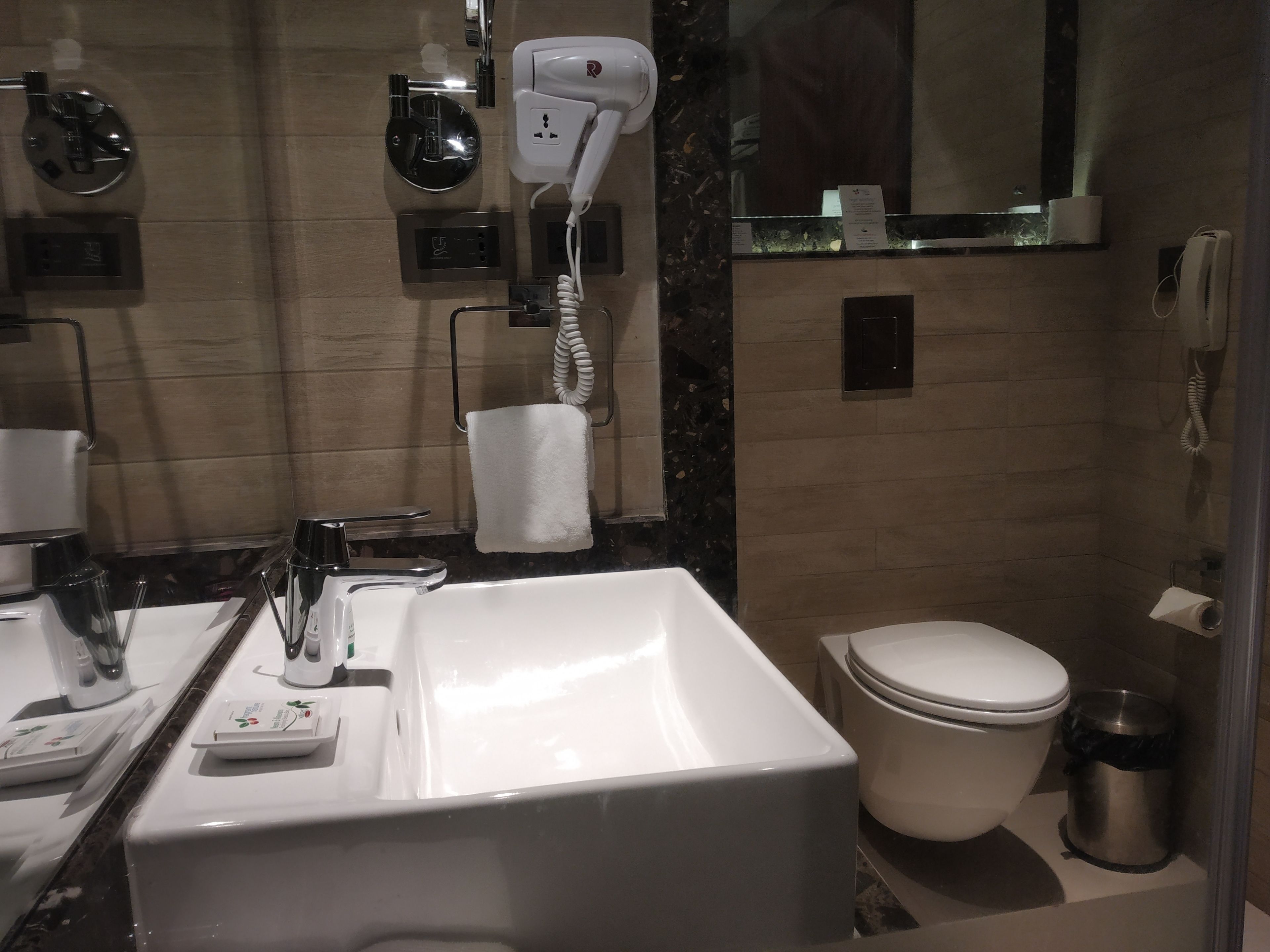 A modern bathroom with a large white sink, a toilet, a hairdryer, and a mirror.