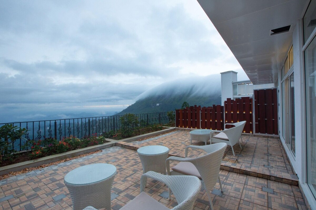 Un balcón con muebles de mimbre, vistas a la montaña y un cielo nublado.