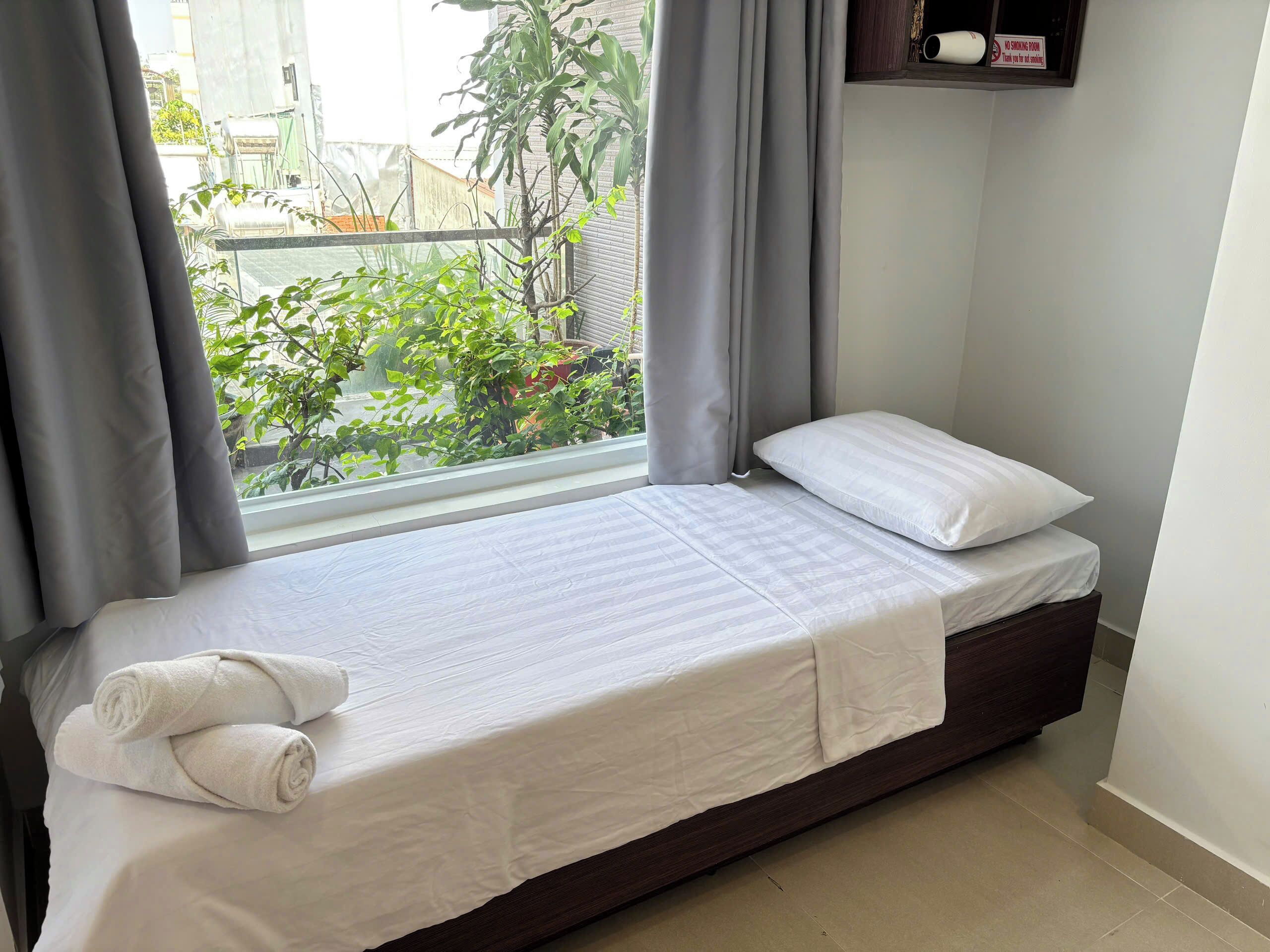 A single bed with white bedding, a dark headboard, and a window with curtains.