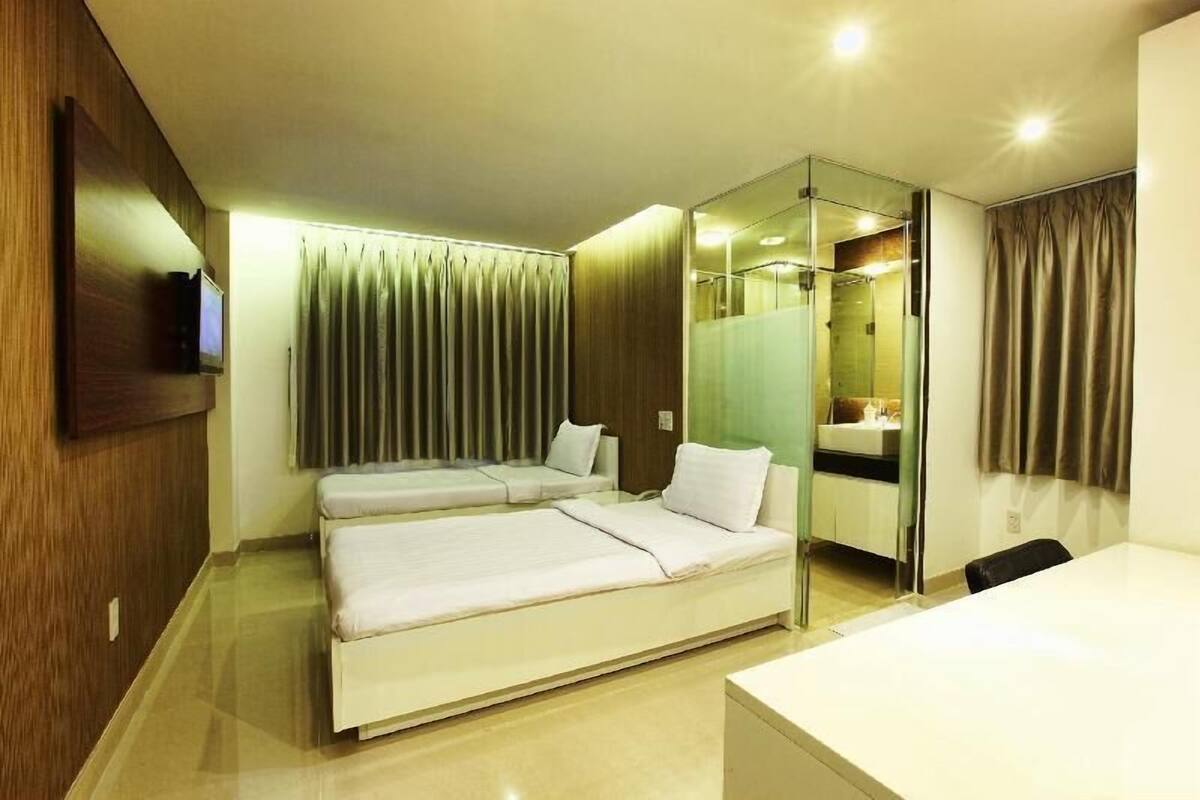 Una habitación de hotel moderna con una cama grande, un escritorio, un espejo y un baño visible a través de una mampara de vidrio.