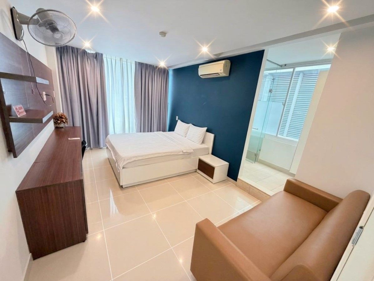 Ein modernes Hotelzimmer mit Bett, Schreibtisch, Stuhl, Ventilator und Blick ins Freie.