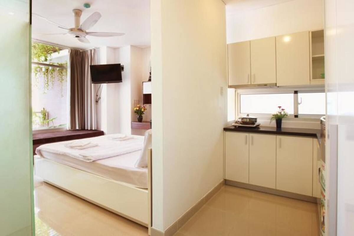 Una habitación de hotel pequeña con una cama, ventilador de techo, televisor y kitchenette con armarios y encimera.