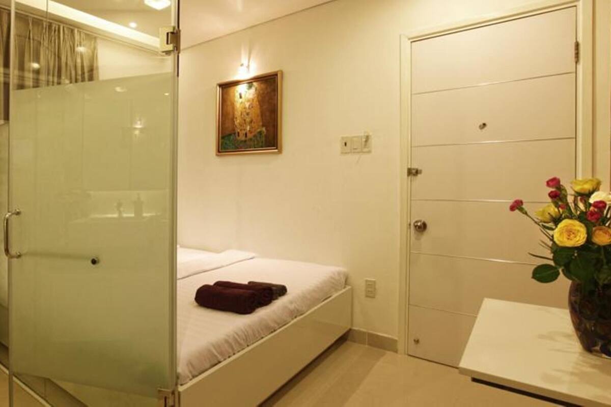Habitación de hotel pequeña con cabina de ducha de vidrio, una cama individual, una mesita de noche y un baño con inodoro.