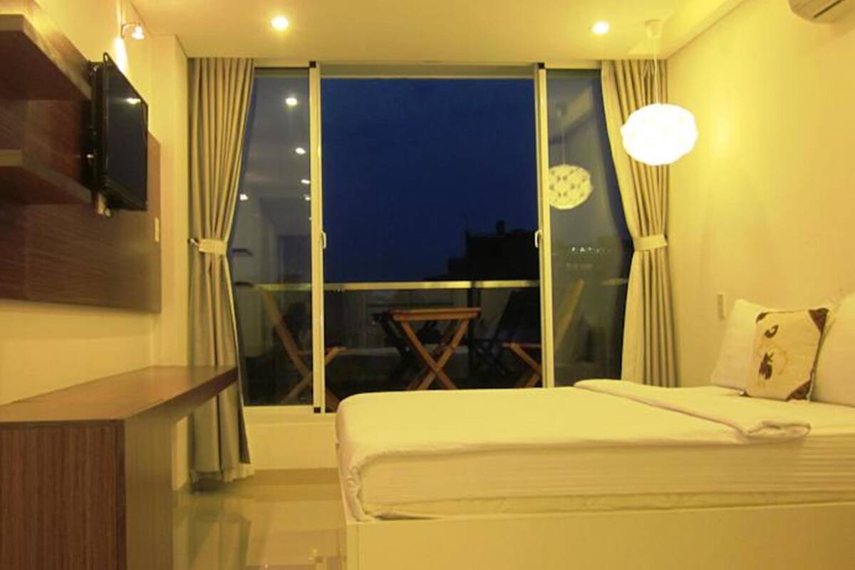 Habitación de hotel con cama, escritorio, silla y balcón con vista a la ciudad de noche.
