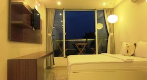 A hotel room with a bed, a desk, a chair, and a balcony with a view of the city at night. - Yellow House Saigon Hotel (Ho Chi Minh City)