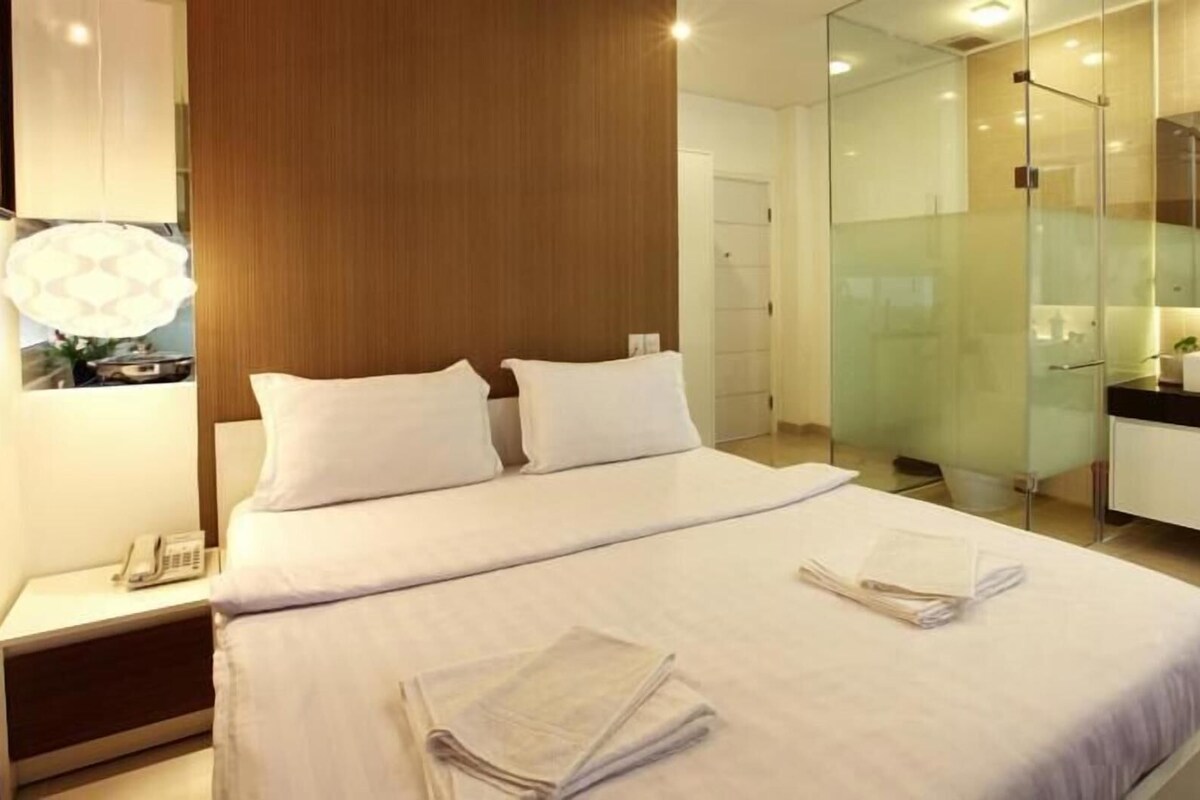 Une chambre d’hôtel moderne dotée d’un grand lit, d’une table de chevet avec un téléphone, d’une douche en verre et d’une salle de bain avec un lavabo et un miroir.