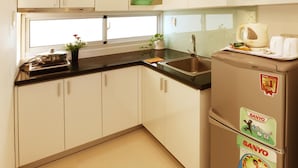 Une cuisine moderne avec des meubles blancs, un plan de travail noir, un évier en acier inoxydable et un réfrigérateur de la marque Sanyo.