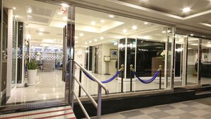 Entrada de hotel con puerta de cristal, una barrera de cuerda azul y una escalera metálica que da al interior.