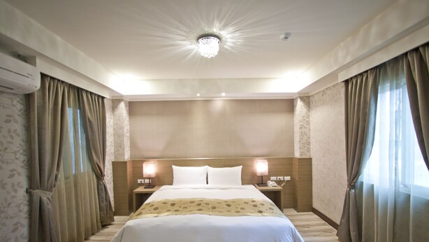 Habitación de hotel con una cama grande, dos mesitas de noche con lámparas, una lámpara de techo y cortinas en las ventanas.