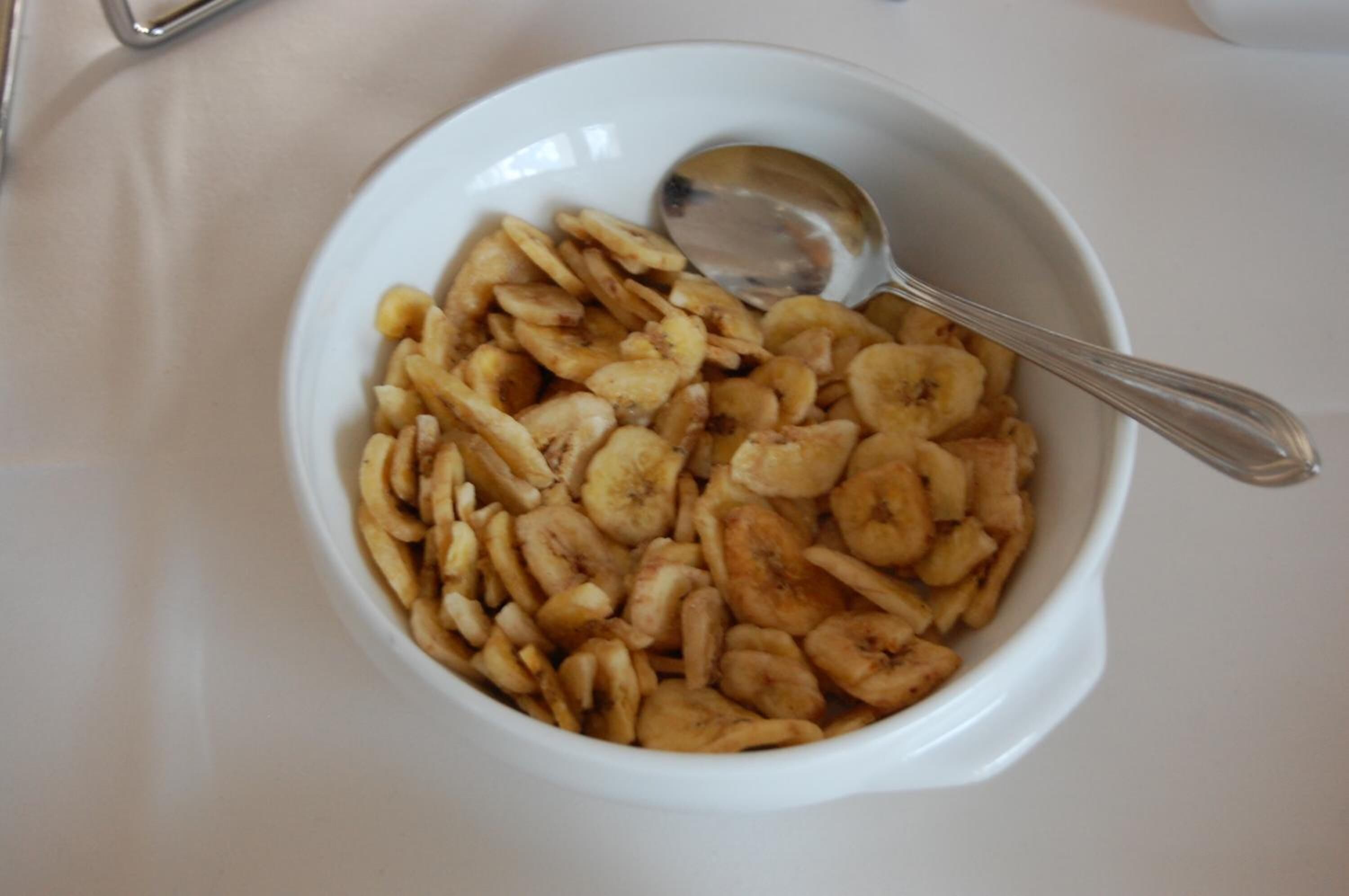 A white bowl filled with dried banana slices and a spoon.