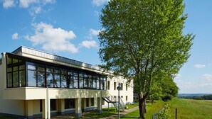 A modern building with large windows, a covered walkway, and a tree in front. - Hotel FIT (Much)