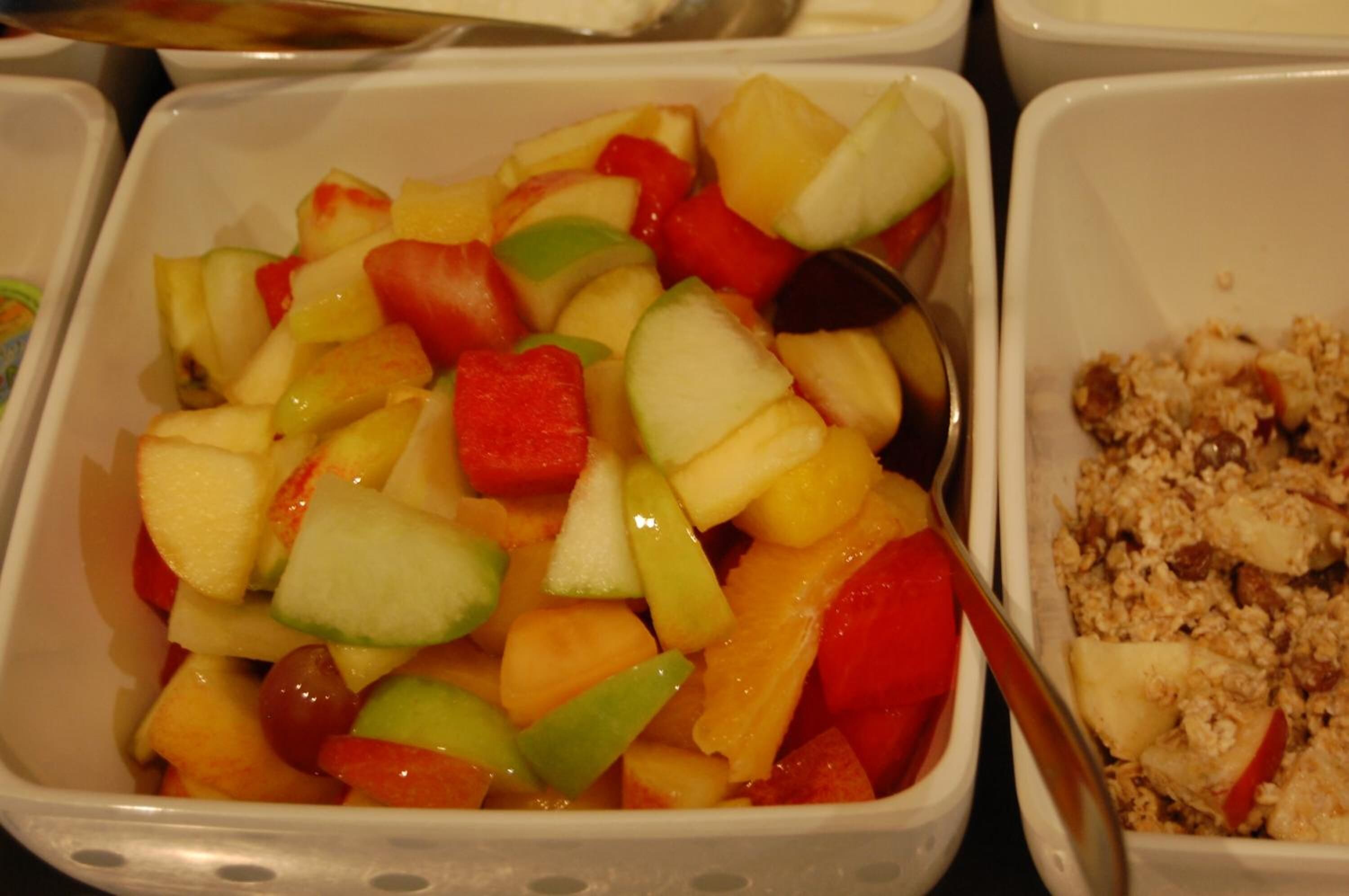 En frugtsalat i en hvid skål med en ske.
