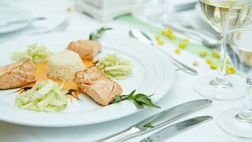 Ein Teller mit Lachs, Reis und Gemüse auf einem weißen Tisch, mit Besteck und einem Glas Weißwein.