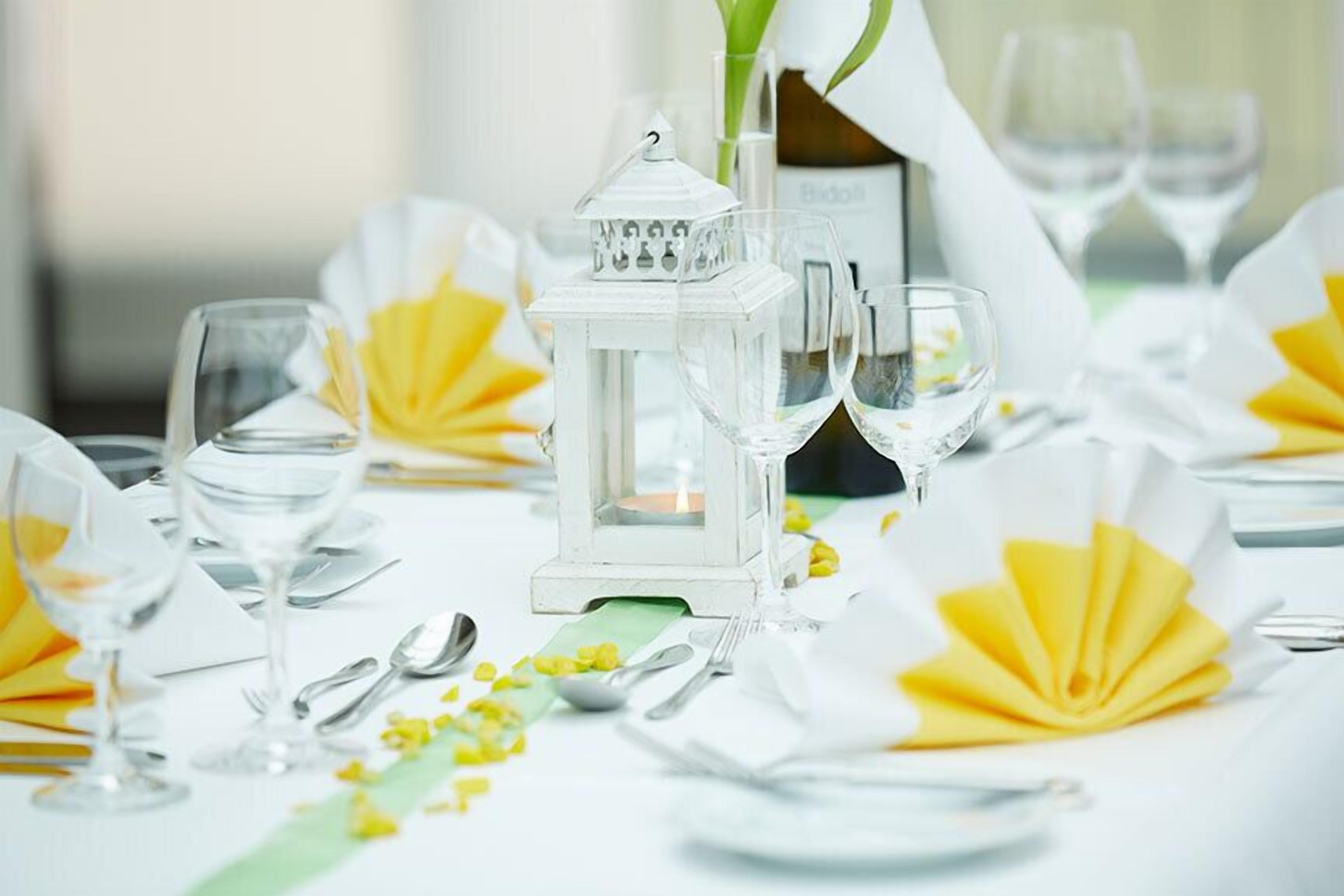 A table set for a formal event with white tablecloths, yellow napkins, clear glassware, and a white lantern centerpiece.