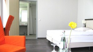 A hotel room with a bed, a nightstand, an orange chair, and a bathroom visible through an open door. - Hotel FIT (Much)