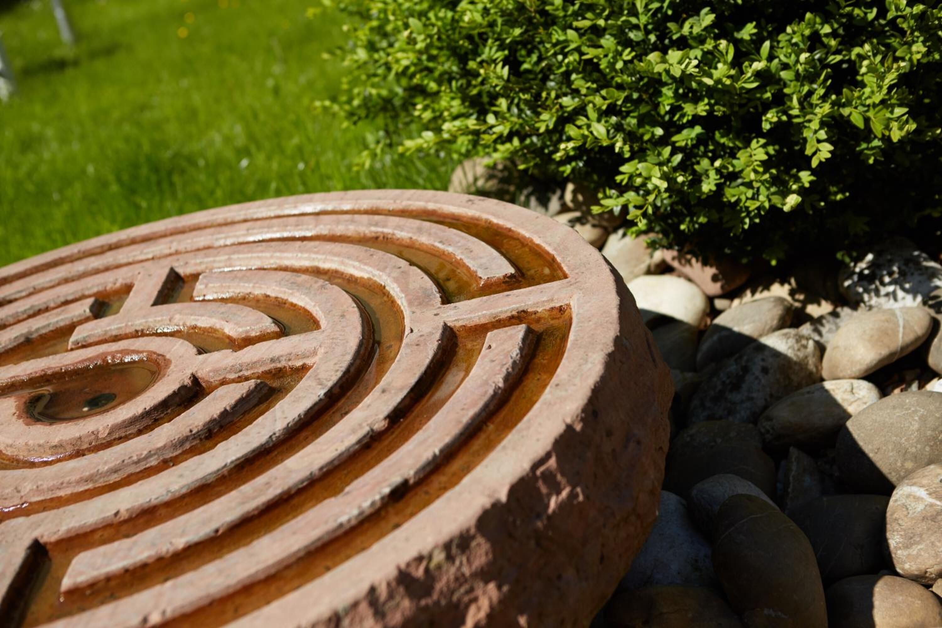 A circular metal structure with concentric rings, surrounded by rocks and greenery.