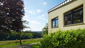 A modern building with large windows and a balcony, surrounded by greenery and a clear sky. - Hotel FIT (Much)