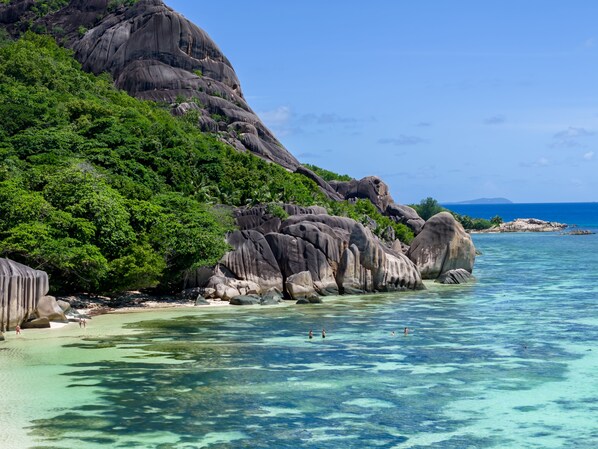 A coastal landscape with clear turquoise waters, rocky formations, and lush greenery.
