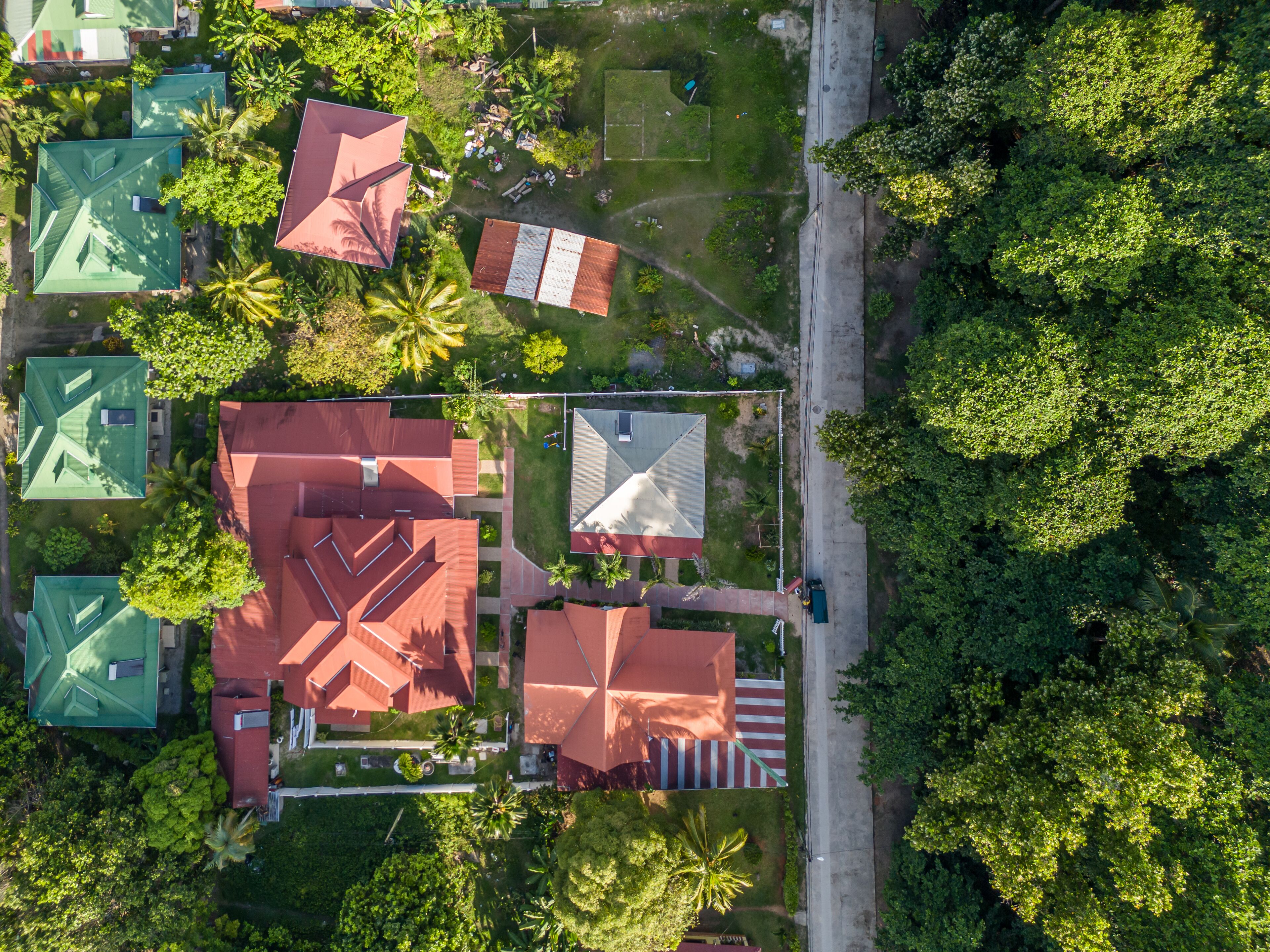 Vista aérea de una zona residencial con varias casas, cada una con un color de tejado diferente. Se observan caminos y una carretera que discurre junto a las viviendas.