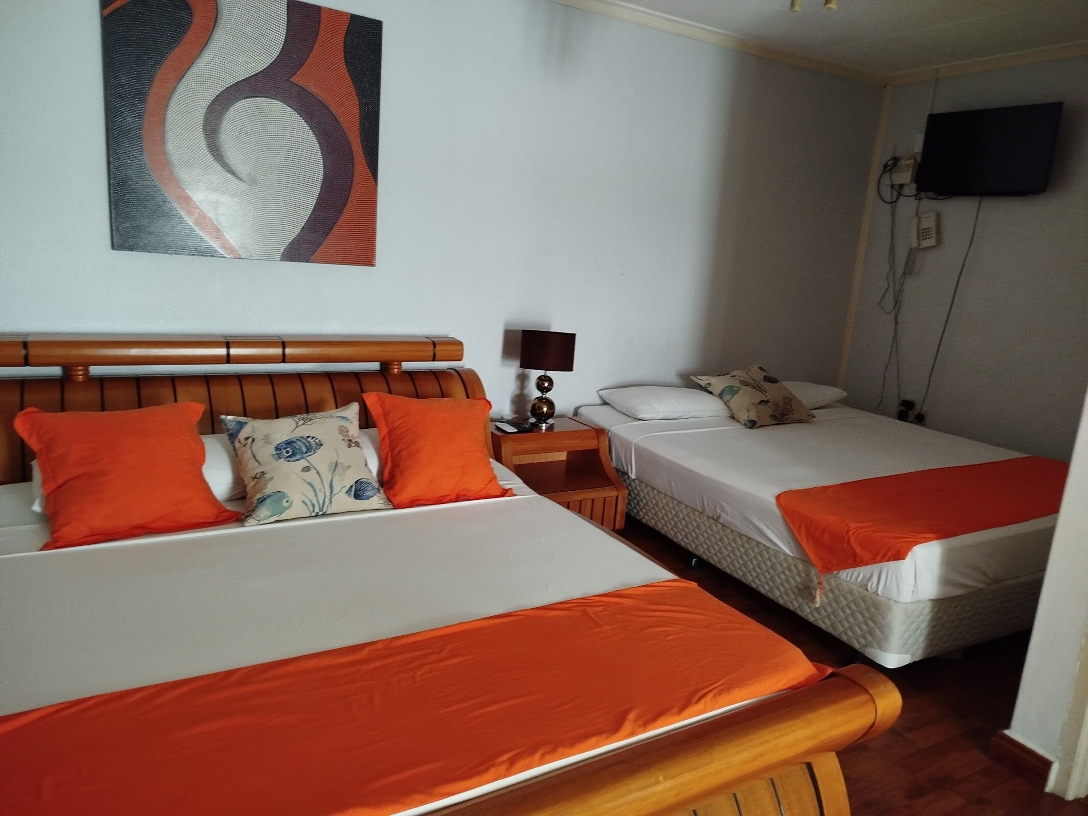 Een hotelkamer met twee bedden, elk met oranje beddengoed, een houten hoofdbord, een nachtkastje met een lamp en een tv aan de muur.