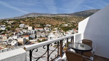 A balcony with wicker chairs and a table, overlooking a town with white buildings and a mountain in the background.