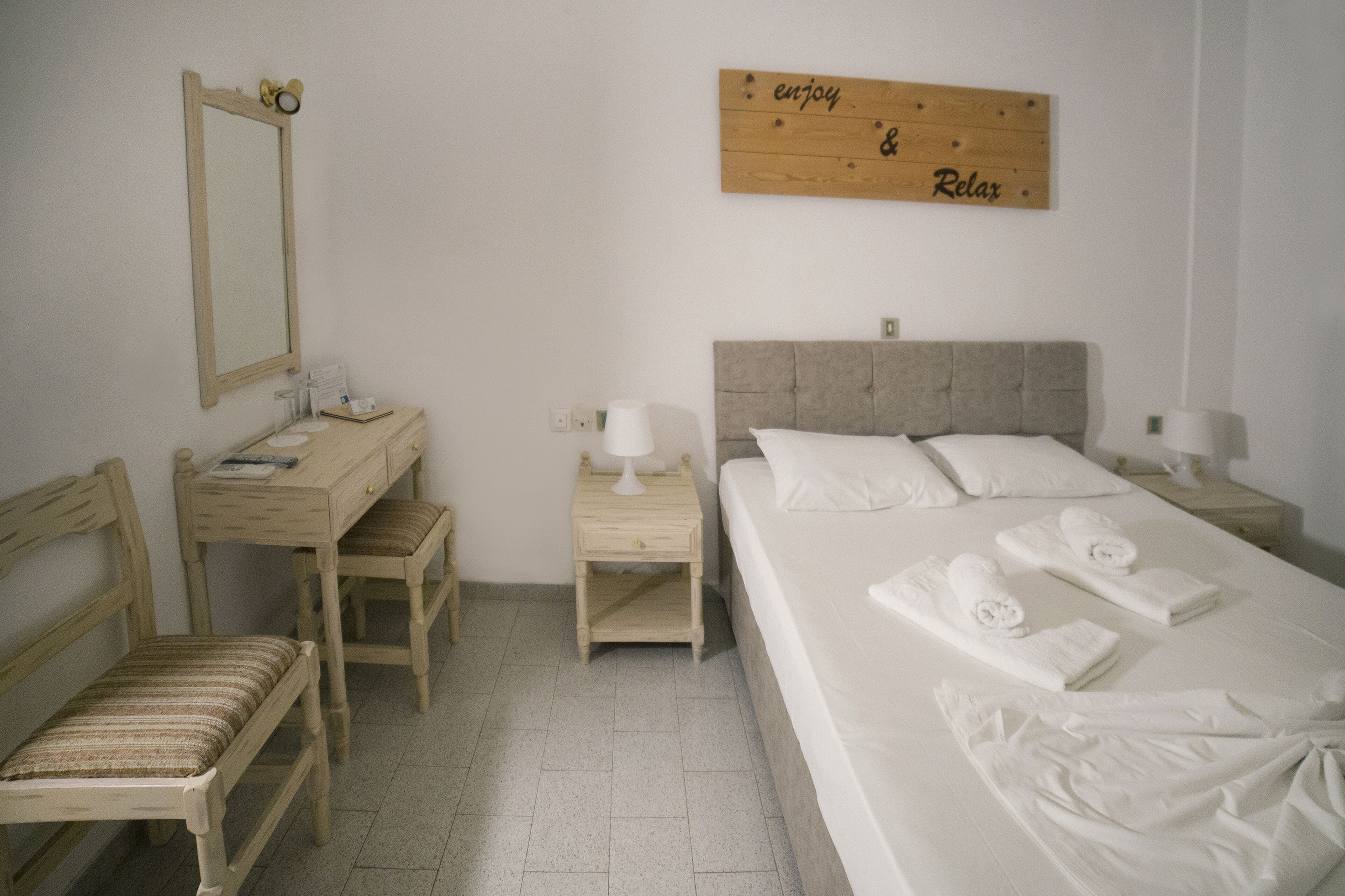 Habitación de hotel con cama, escritorio, silla, mesita de noche, espejo y cartel en la pared.