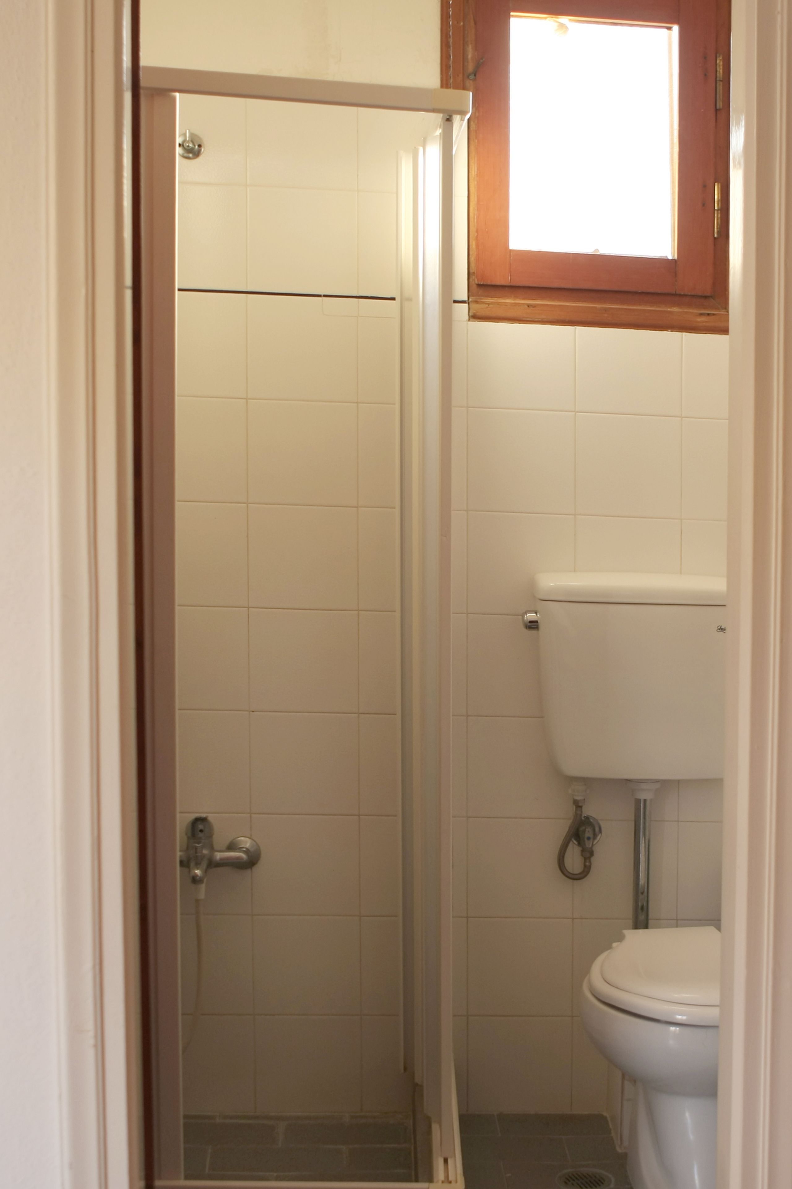 Un baño con ducha, inodoro y ventana sobre el inodoro.