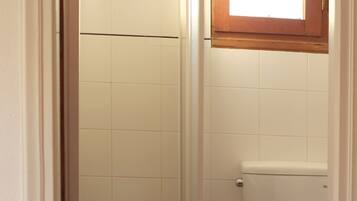 Un baño con ducha, inodoro y ventana sobre el inodoro.