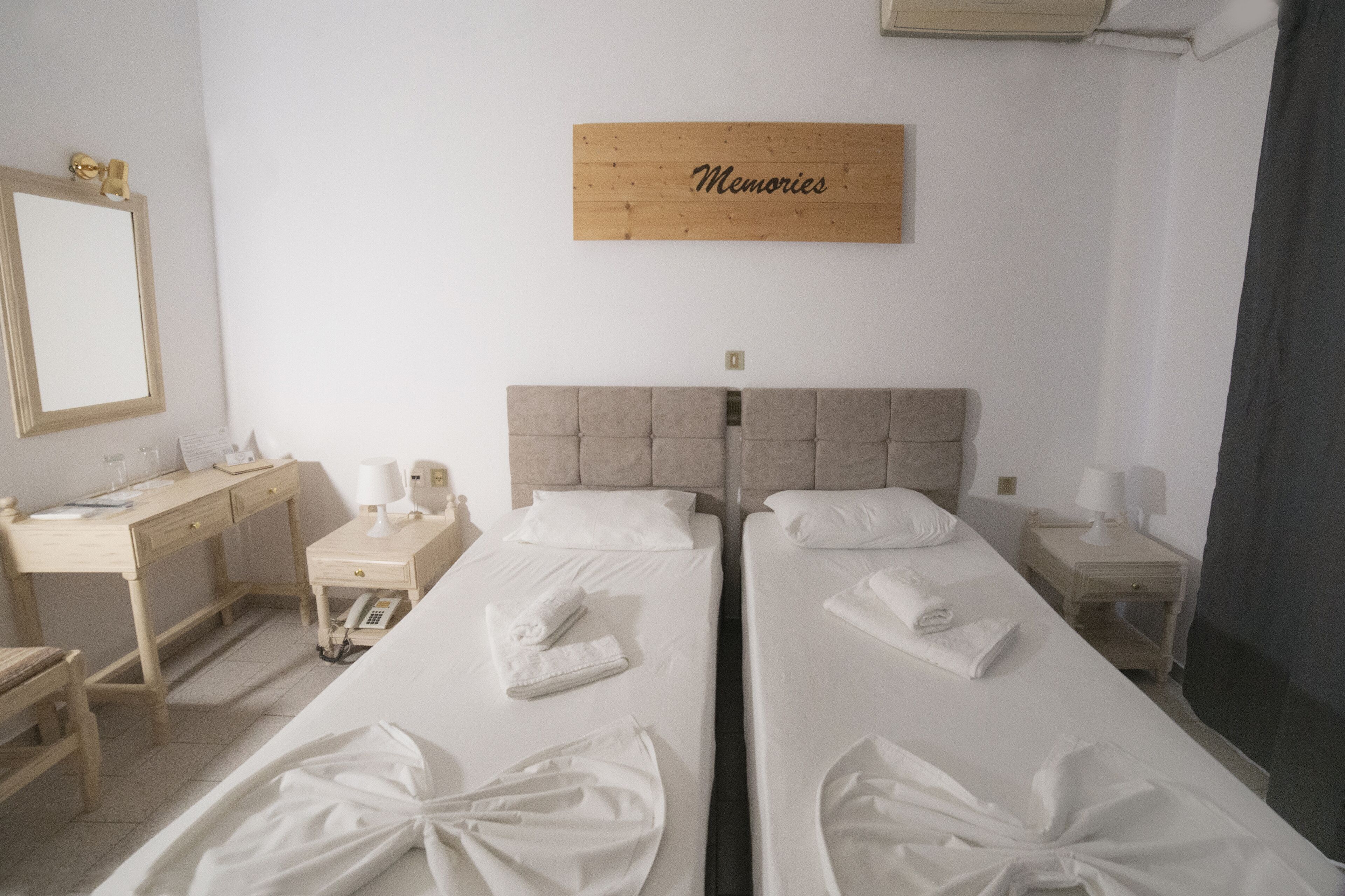 Habitación de hotel con dos camas, un escritorio, una silla y un espejo, y un cartel que dice "Memories".