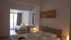 A hotel room with a large bed, a bedside table with a lamp, a mirror, and a wooden sign on the wall. - Kastro Hotel (Ikaria)