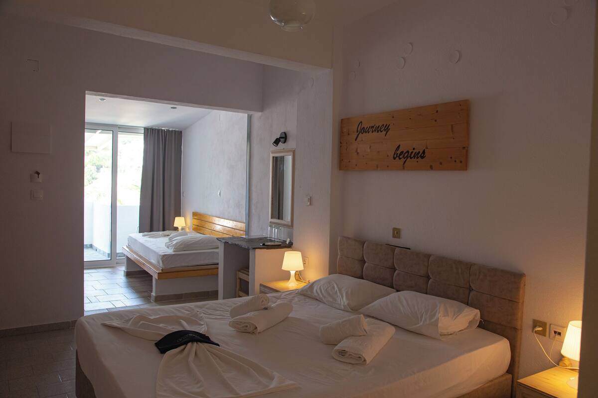 Habitación de hotel con una cama grande, una mesita de noche con lámpara, un espejo y un cartel de madera en la pared.