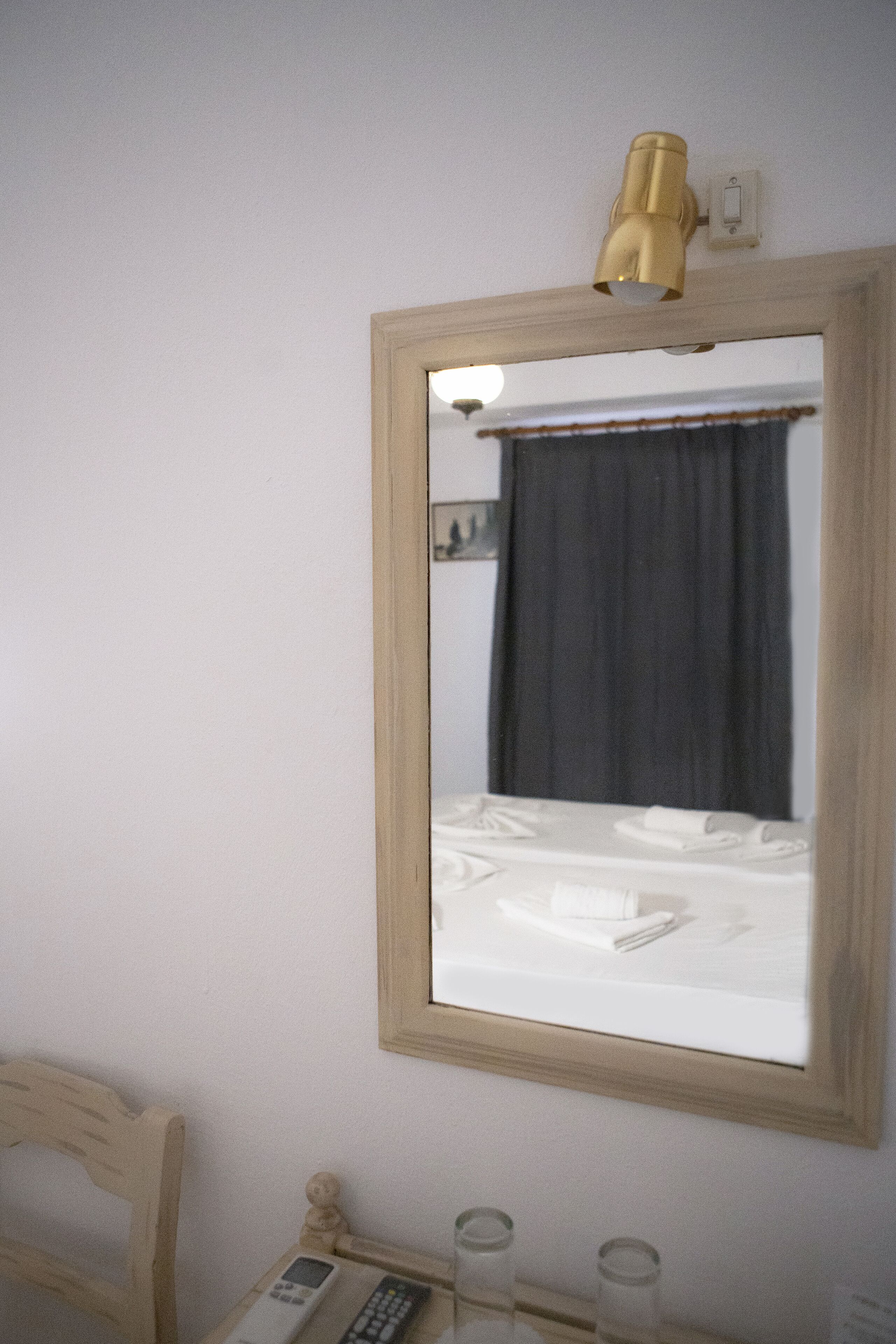 Een slaapkamer met een bed, een nachtkastje met een lamp, een stoel en een spiegel aan de muur.