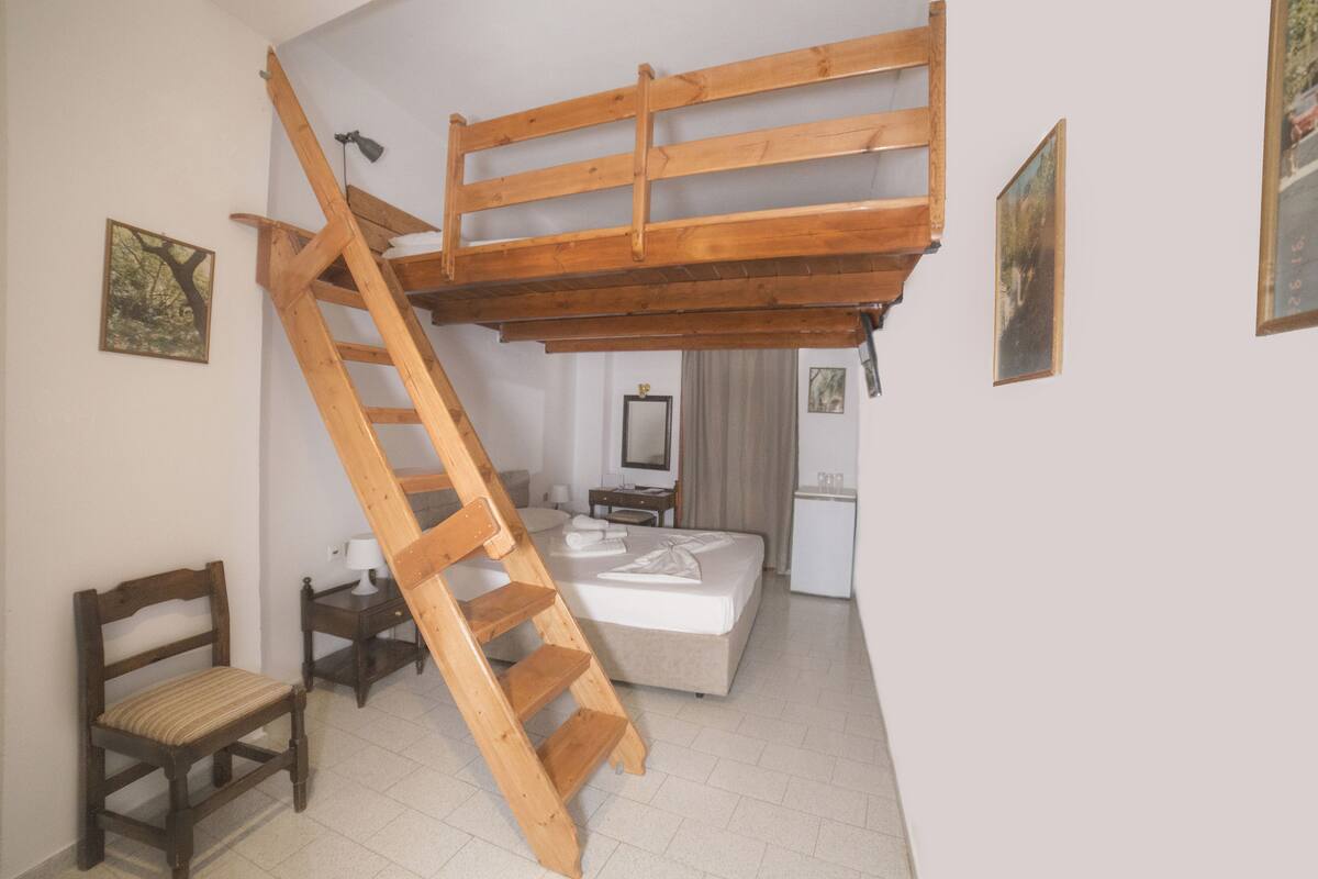 Un dormitorio con una cama litera, una escalera de madera, una mesita de noche, una silla y un escritorio pequeño.
