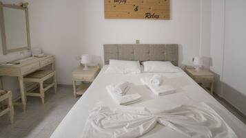 Una cama bien hecha con sábanas y toallas blancas, un cabecero de madera, mesitas de noche con lámparas y un espejo en la pared.
