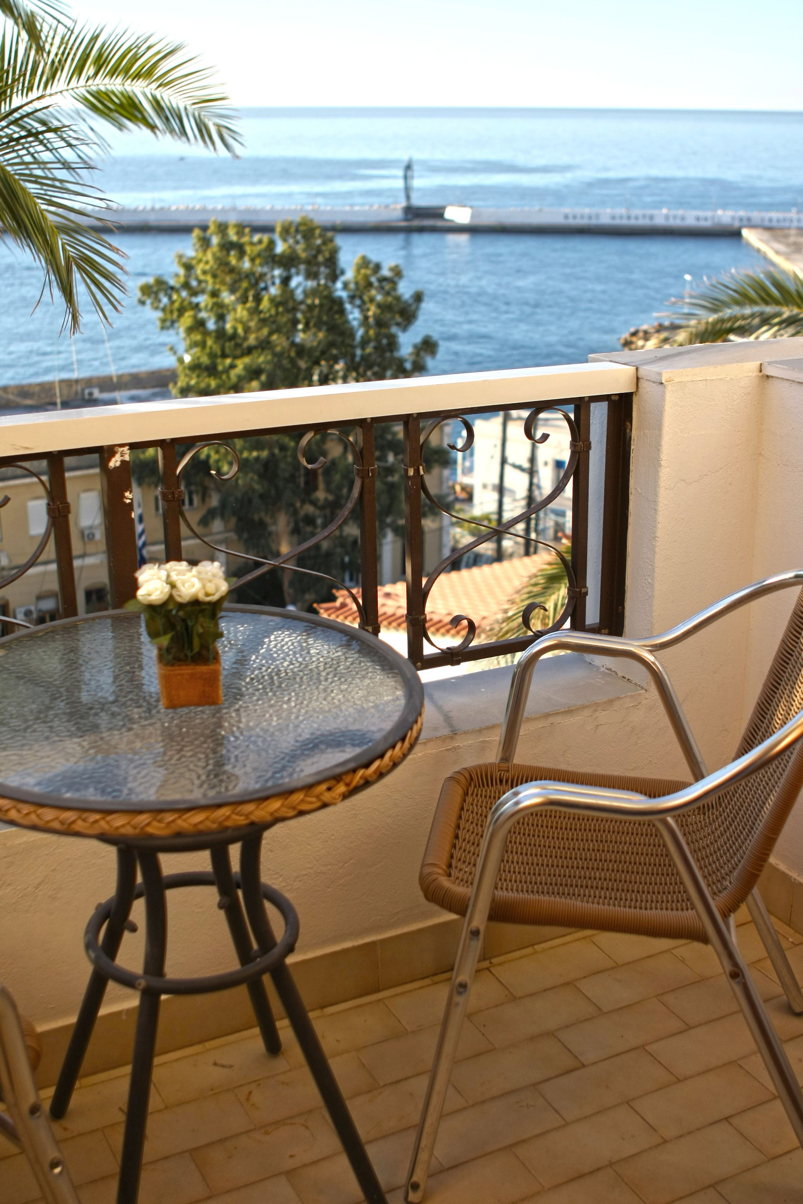 A balcony with a round glass table, a wicker chair, and a potted plant.