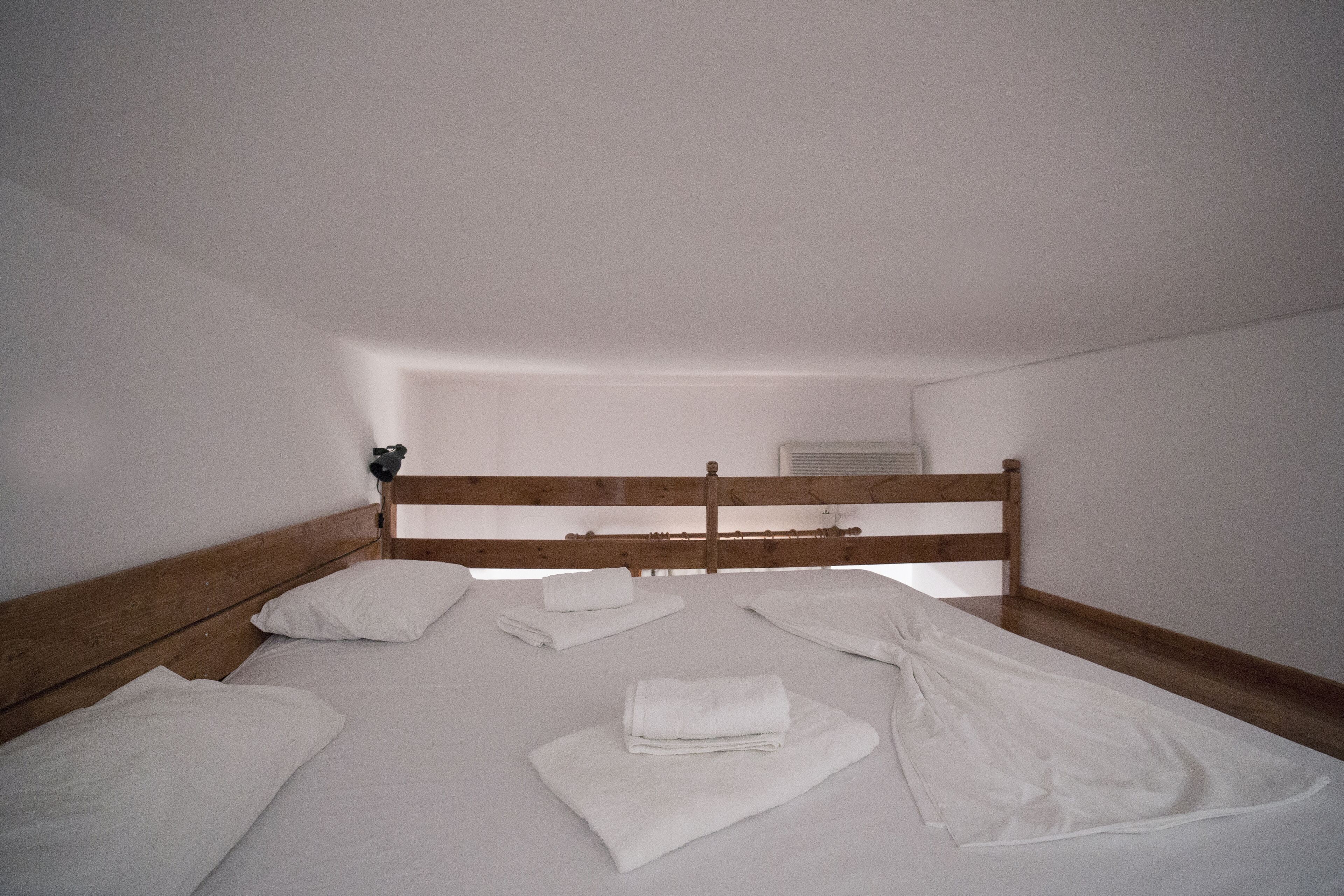 Een slaapkamer met een houten hoofdbord, witte lakens en een netjes opgemaakt bed.