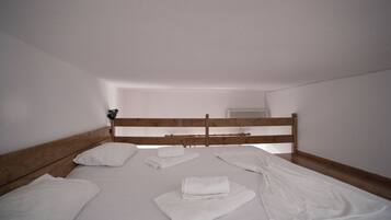 Een slaapkamer met een houten hoofdbord, witte lakens en een netjes opgemaakt bed.