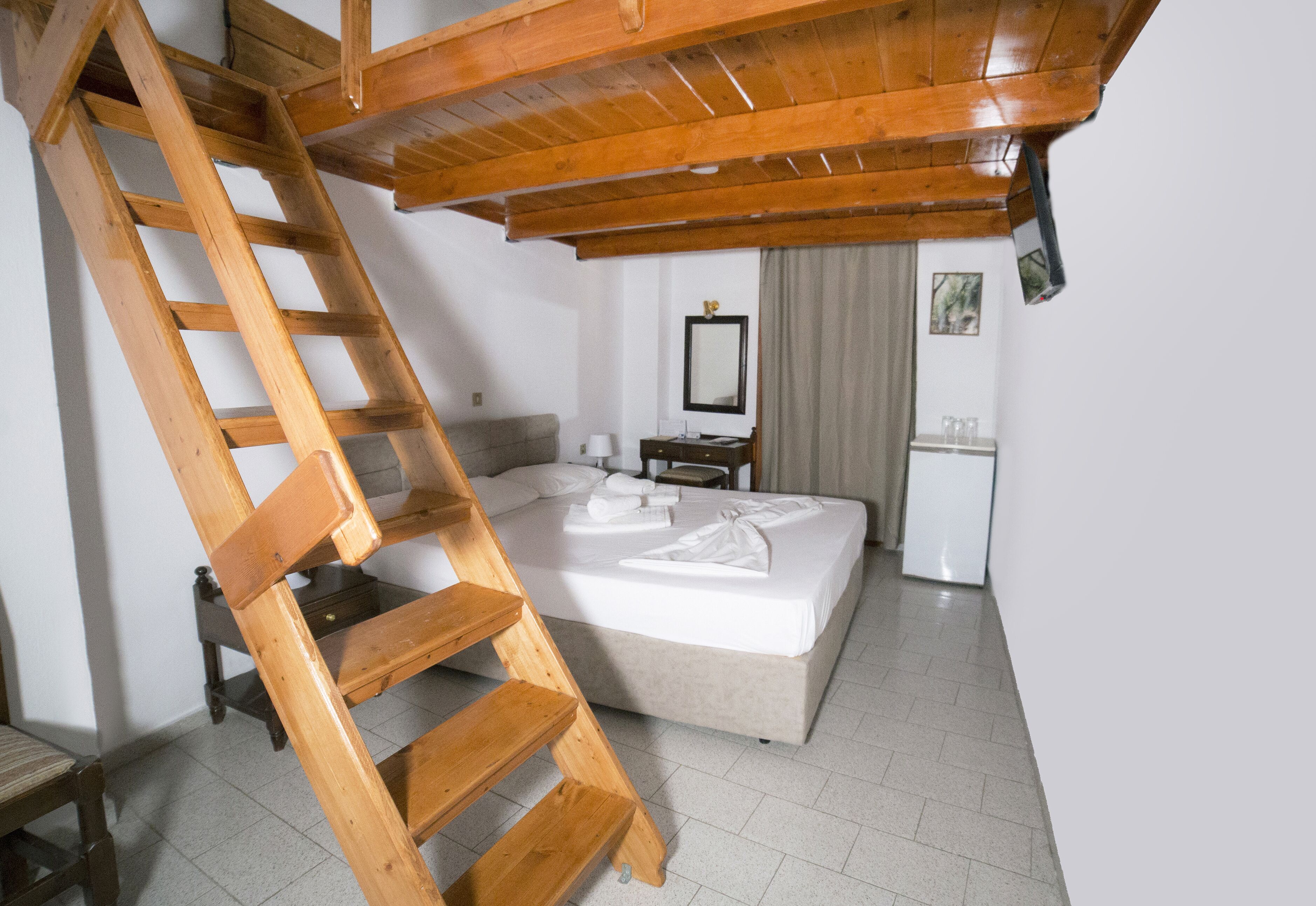 A bedroom with a wooden ladder, a bed with neatly arranged towels, a bedside table, and a mirror on the wall.