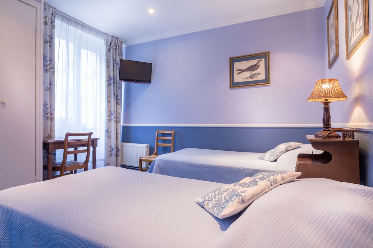 Une chambre d’hôtel avec deux lits, un bureau, une chaise, une télévision et une lampe.