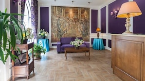 Une pièce dotée d’un parquet en bois à motifs en chevrons, d’un canapé violet, d’une table basse en bois et d’une grande tapisserie murale.