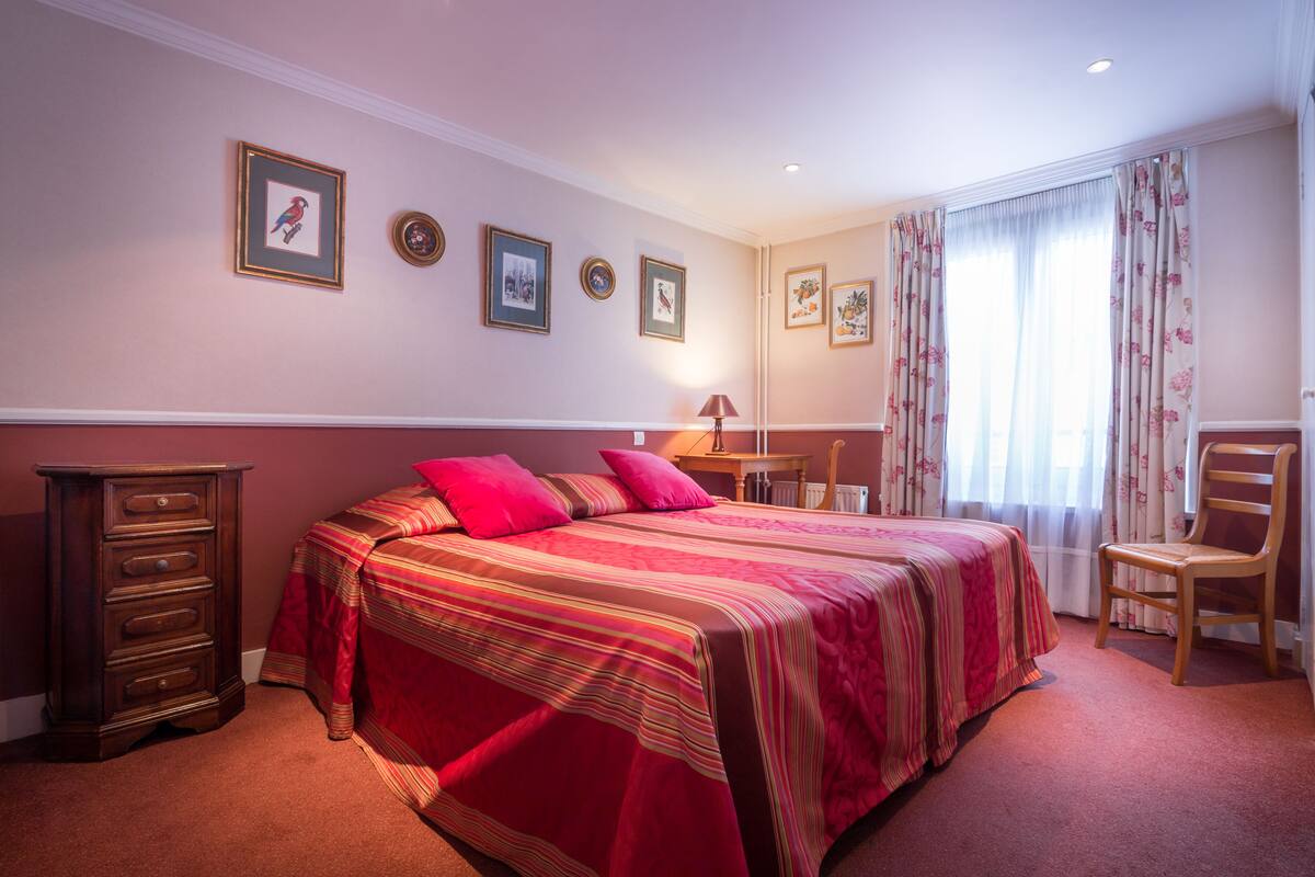 Une chambre à coucher avec un lit, une commode, une chaise et des tableaux encadrés accrochés au mur.